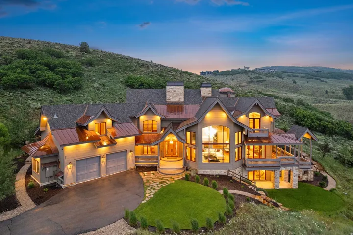 Custom-built residence featuring copper roofing details, stone accents, multiple balconies, a paver driveway, and an attached two-car garage