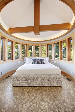 Curved wall with a continuous band of wood-framed windows, exposed timber ceiling beams, and a light-toned patterned floor