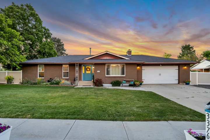 Brick exterior featuring a two-car garage, mature front lawn, and landscaped garden beds