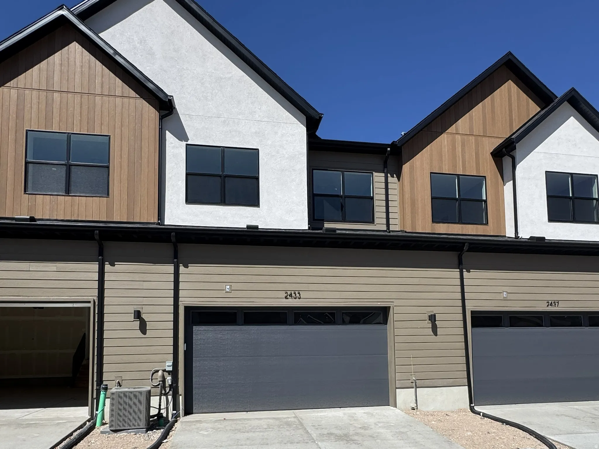 Contemporary townhome exterior featuring a stucco facade, wood-finish siding, black frame windows, and a dark gray garage door