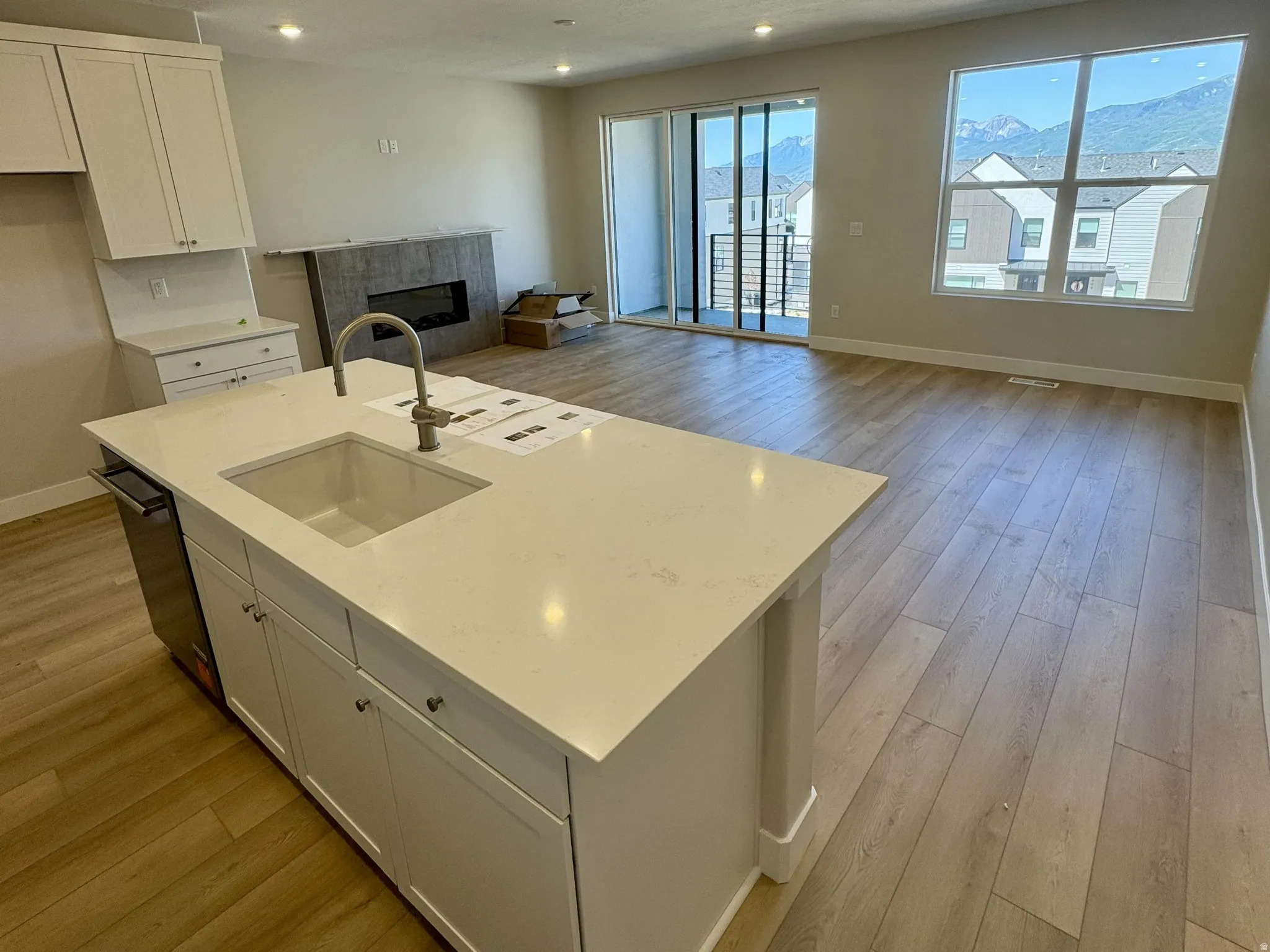 Open-concept living area featuring a kitchen island with integrated sink, stainless steel dishwasher, wood-finish flooring, and a fireplace with a stone surround