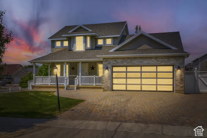 Traditional two-story residence featuring a covered front porch with white railing, a stone-accented garage facade, a modern sectional garage door, a paved driveway, and a manicured front lawn