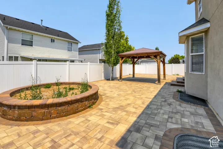 Spacious paver patio featuring a wooden gazebo with a metal roof, a raised stone planter, and a white vinyl privacy fence