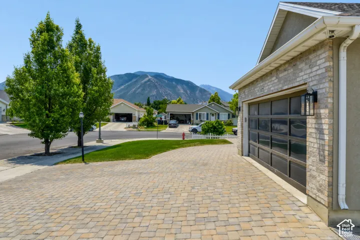 Paver driveway with a multi-paneled garage door, brick and stucco exterior, and wall-mounted exterior lighting