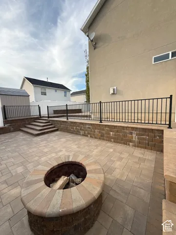 Paver patio featuring a built-in fire pit, tiered paver steps, and retaining walls with black metal railing