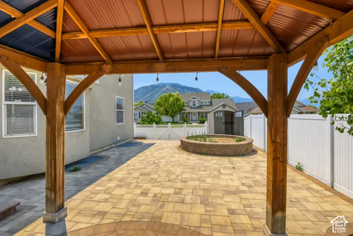 Expansive paver patio featuring a wooden gazebo with metal roofing, a built-in stone fire pit, and a white privacy fence