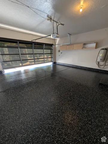 Epoxy-coated garage flooring, glass panel garage door, automatic garage door opener, overhead wall-mounted cabinetry, and wall-mounted utility hookups