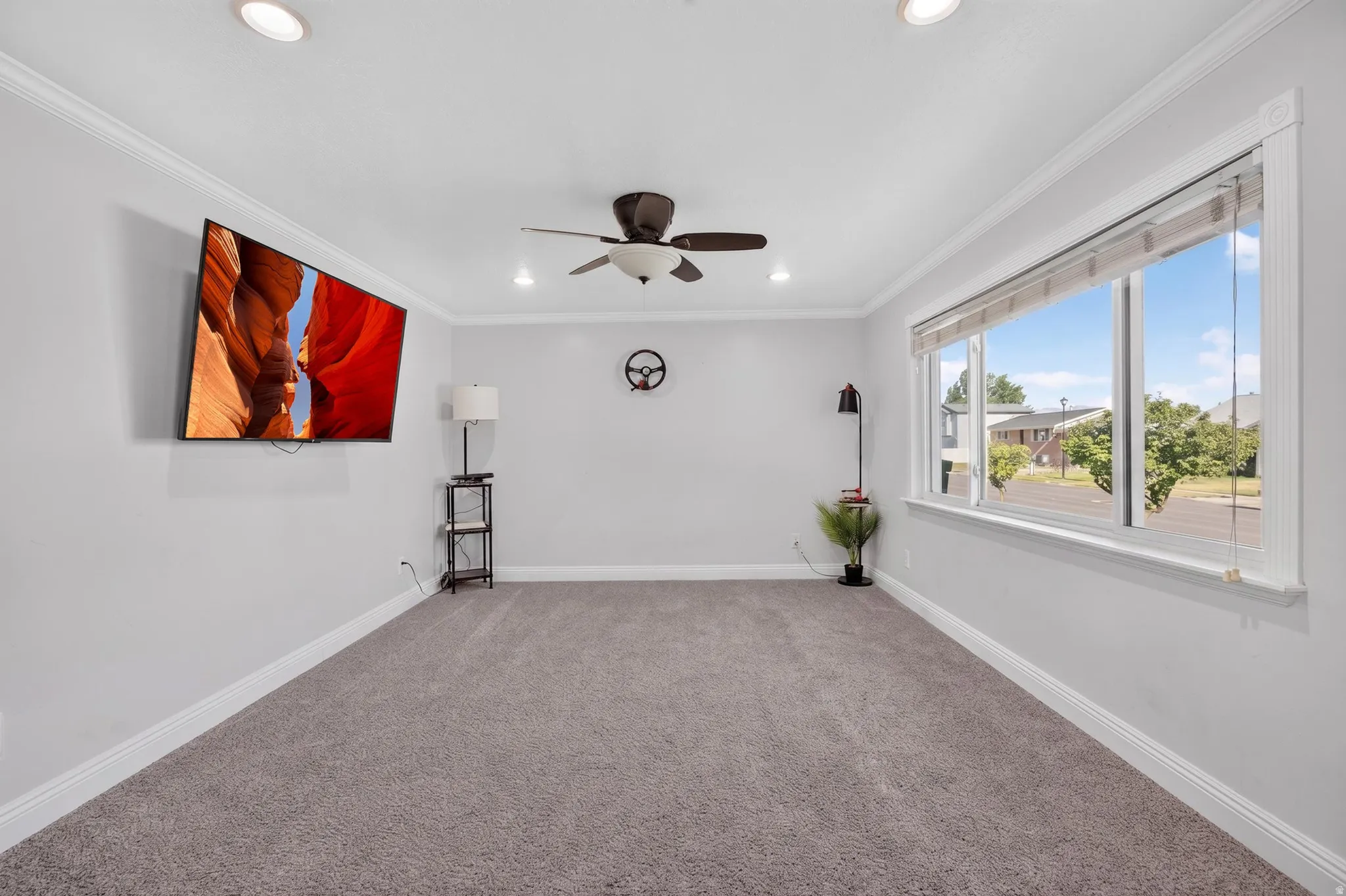 Spacious room featuring light gray walls, plush gray carpeting, white crown molding, and recessed lighting