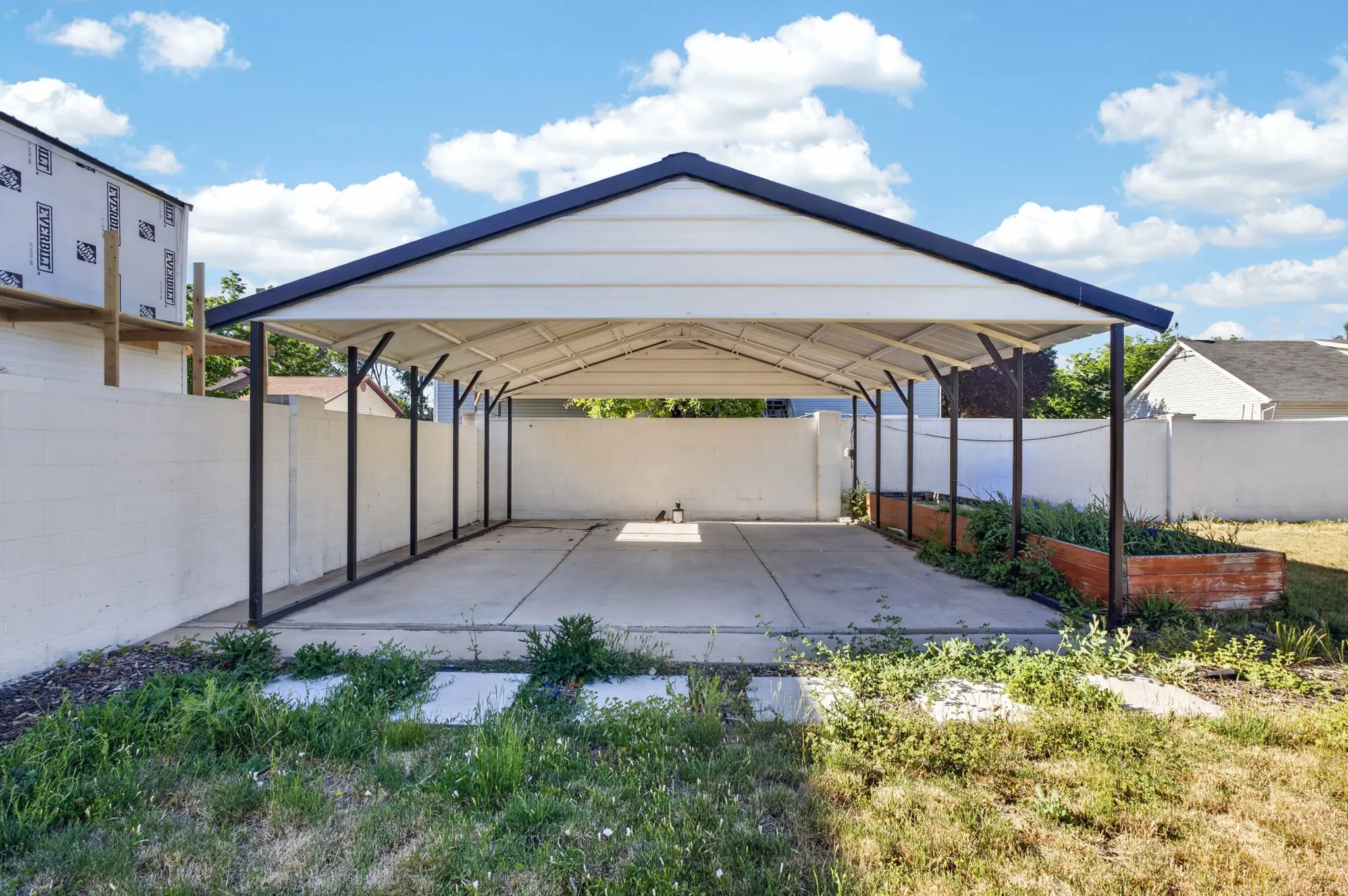 Covered parking structure with a concrete pad and white siding