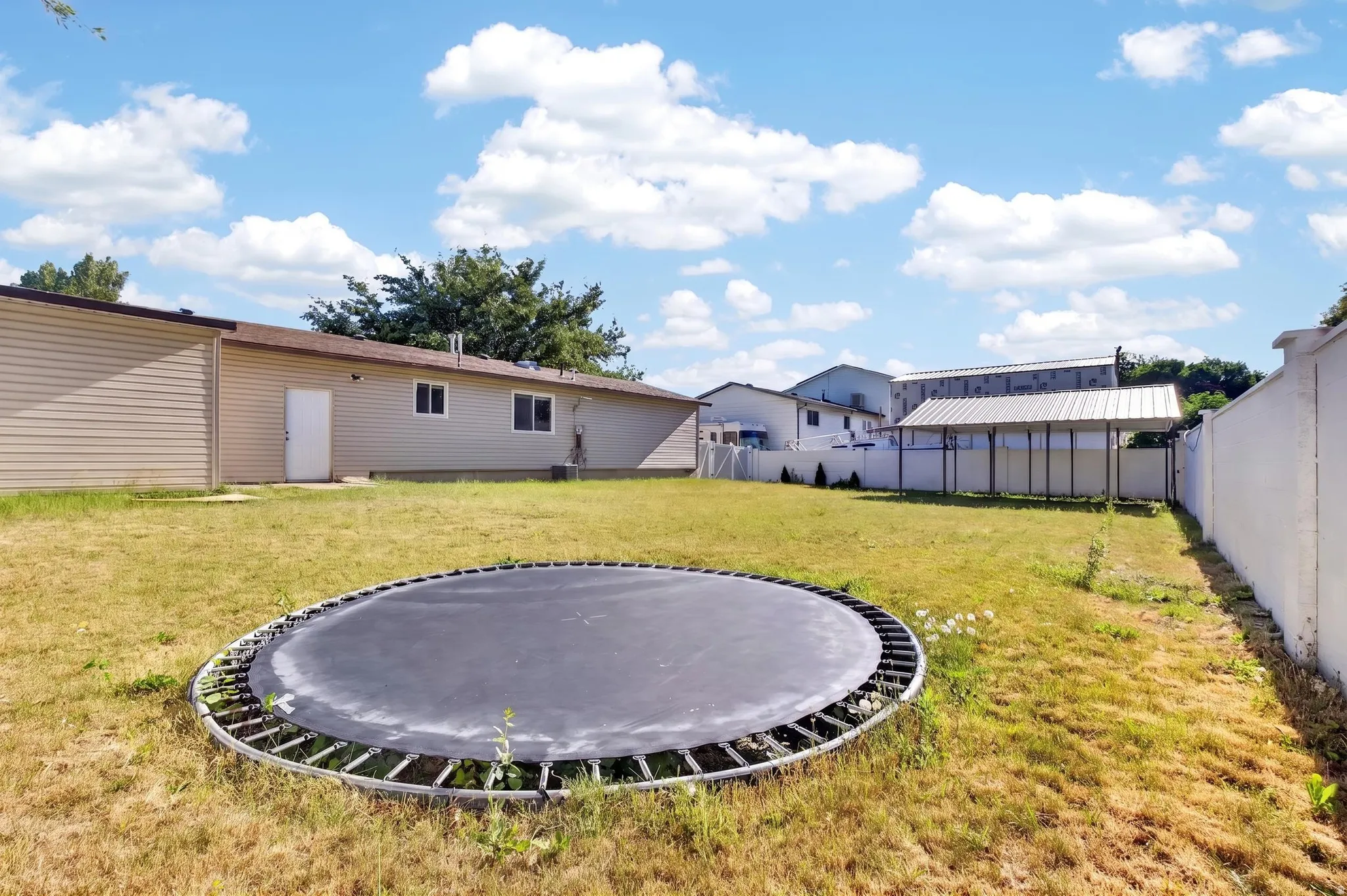 Expansive backyard featuring a large grassy area, a covered structure, and a perimeter wall