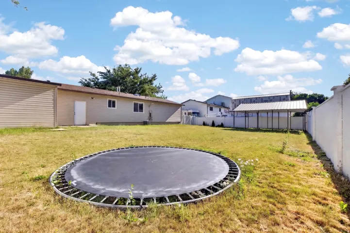 Expansive backyard featuring a large grassy area, a covered structure, and a perimeter wall