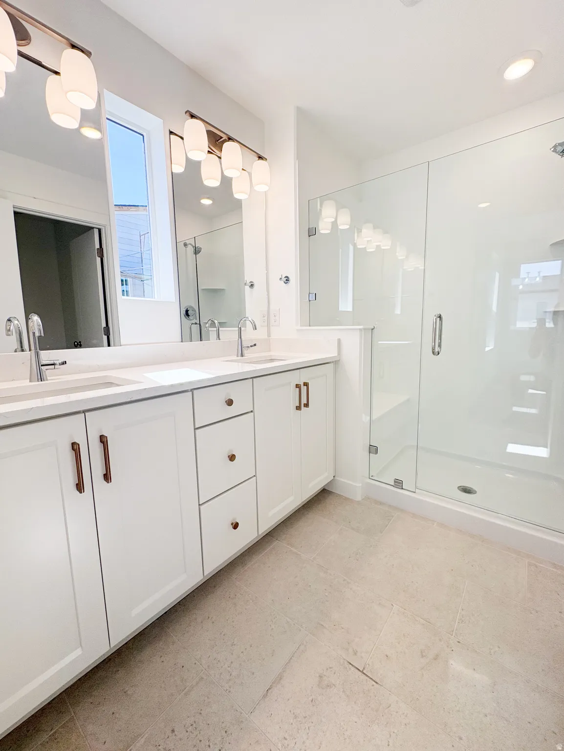 Double vanity featuring white shaker cabinetry with bronze hardware, dual sinks, and a light-toned countertop