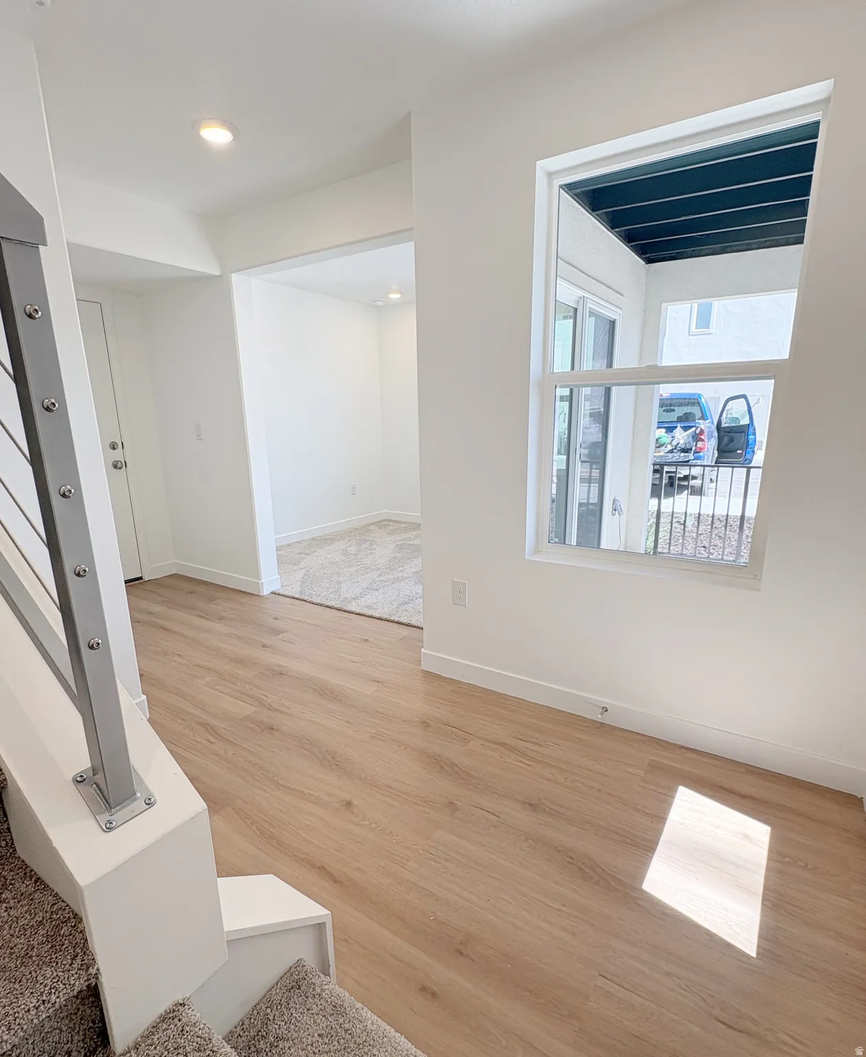 Bright interior featuring light wood-finish flooring, white walls, and a modern staircase with a metal railing
