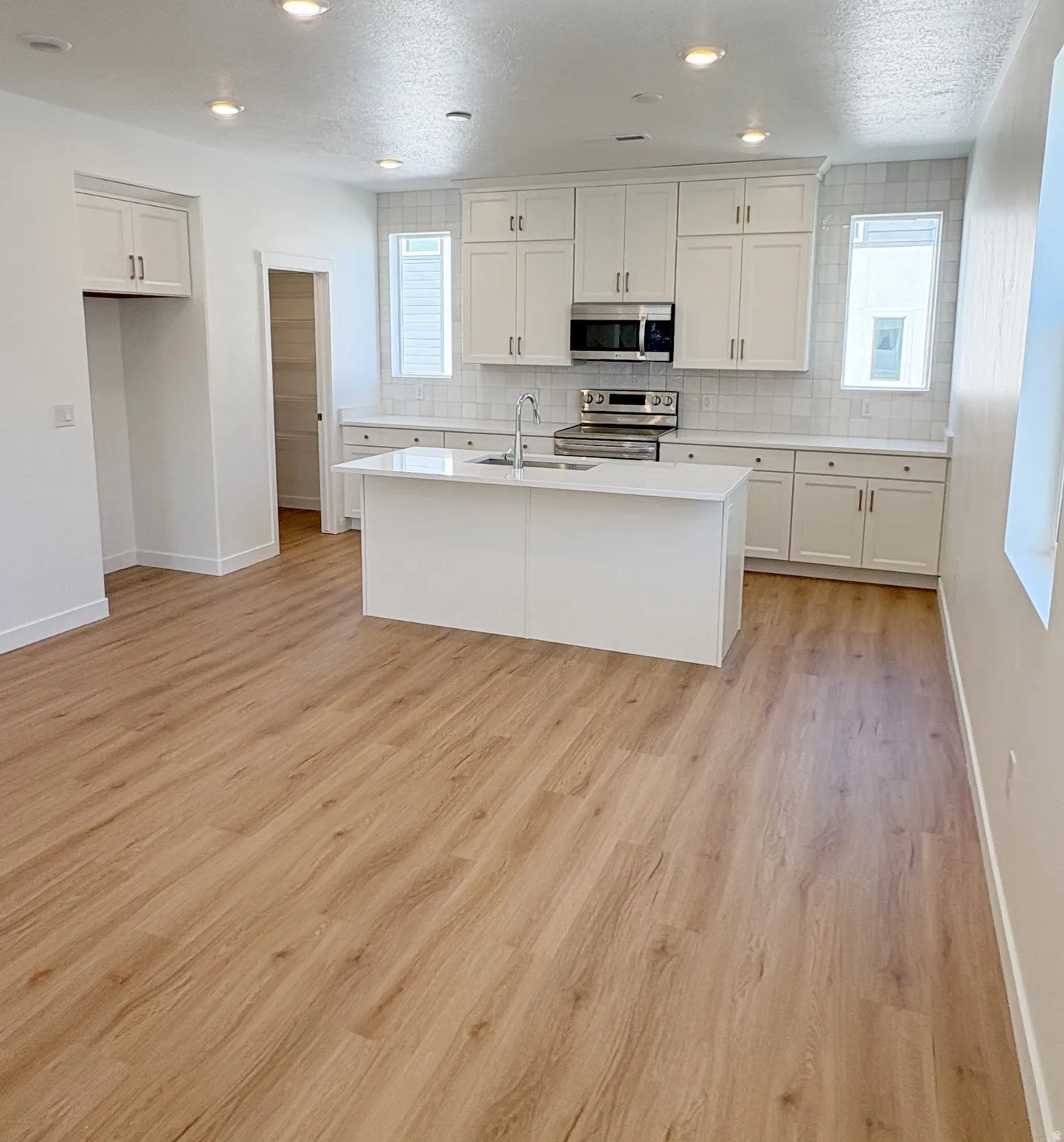 Contemporary kitchen featuring white cabinetry, stainless steel appliances, a center island with an integrated sink, white subway tile backsplash, and wood-finish flooring