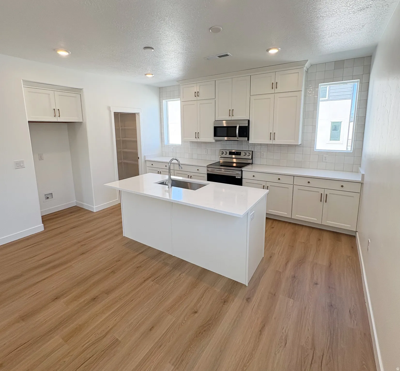 Modern kitchen featuring a large central island with an undermount sink, white quartz countertops, and white shaker cabinetry
