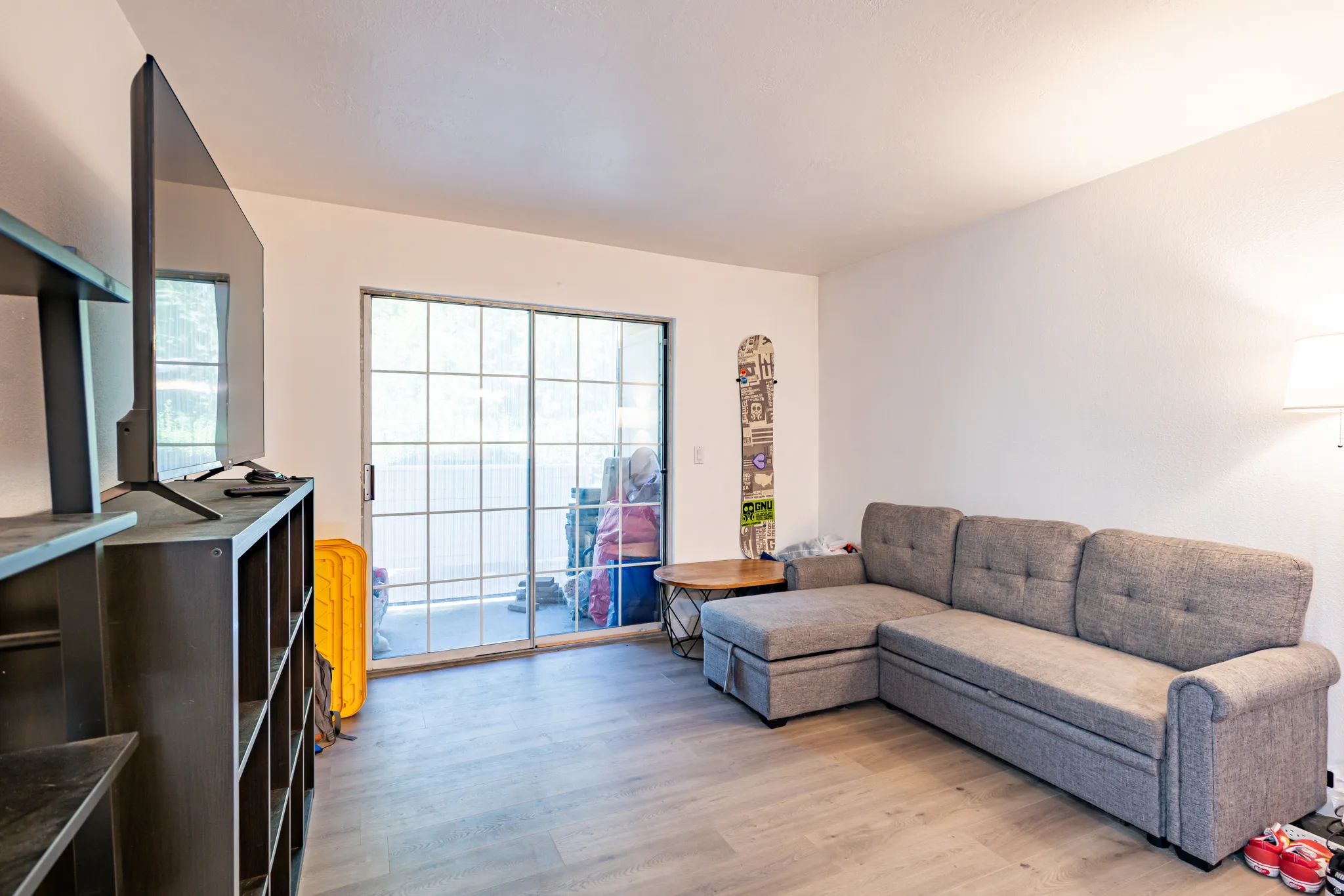 Spacious room featuring light wood-finish flooring, white painted walls, and a large grid-patterned sliding glass door opening to an exterior area