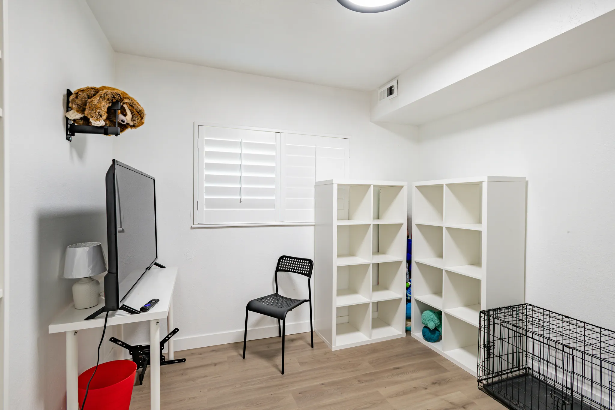 Versatile room with wood-finish flooring, white walls, and a window featuring plantation shutters
