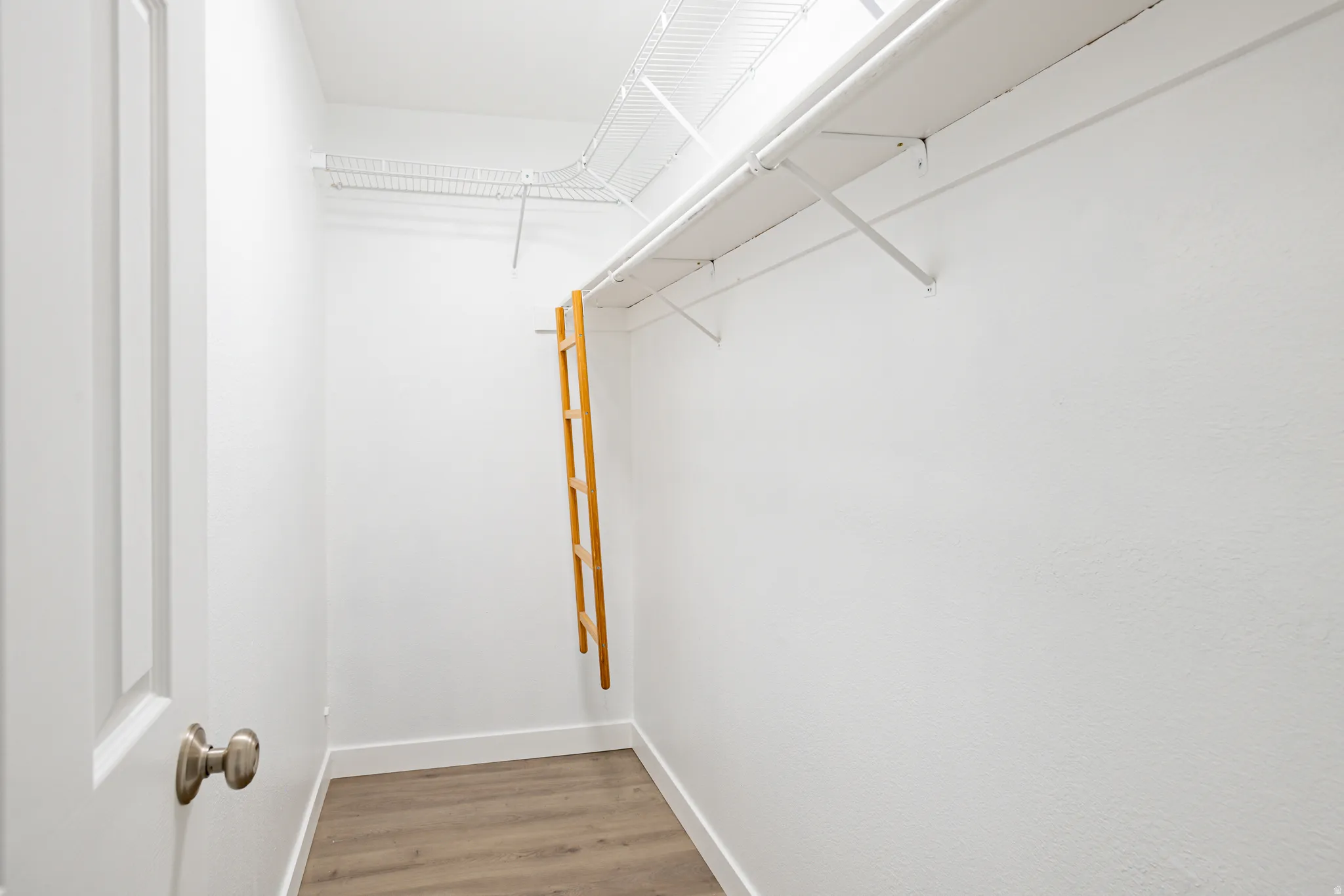 Walk-in closet featuring wood-finish flooring, white walls, and built-in wire shelving