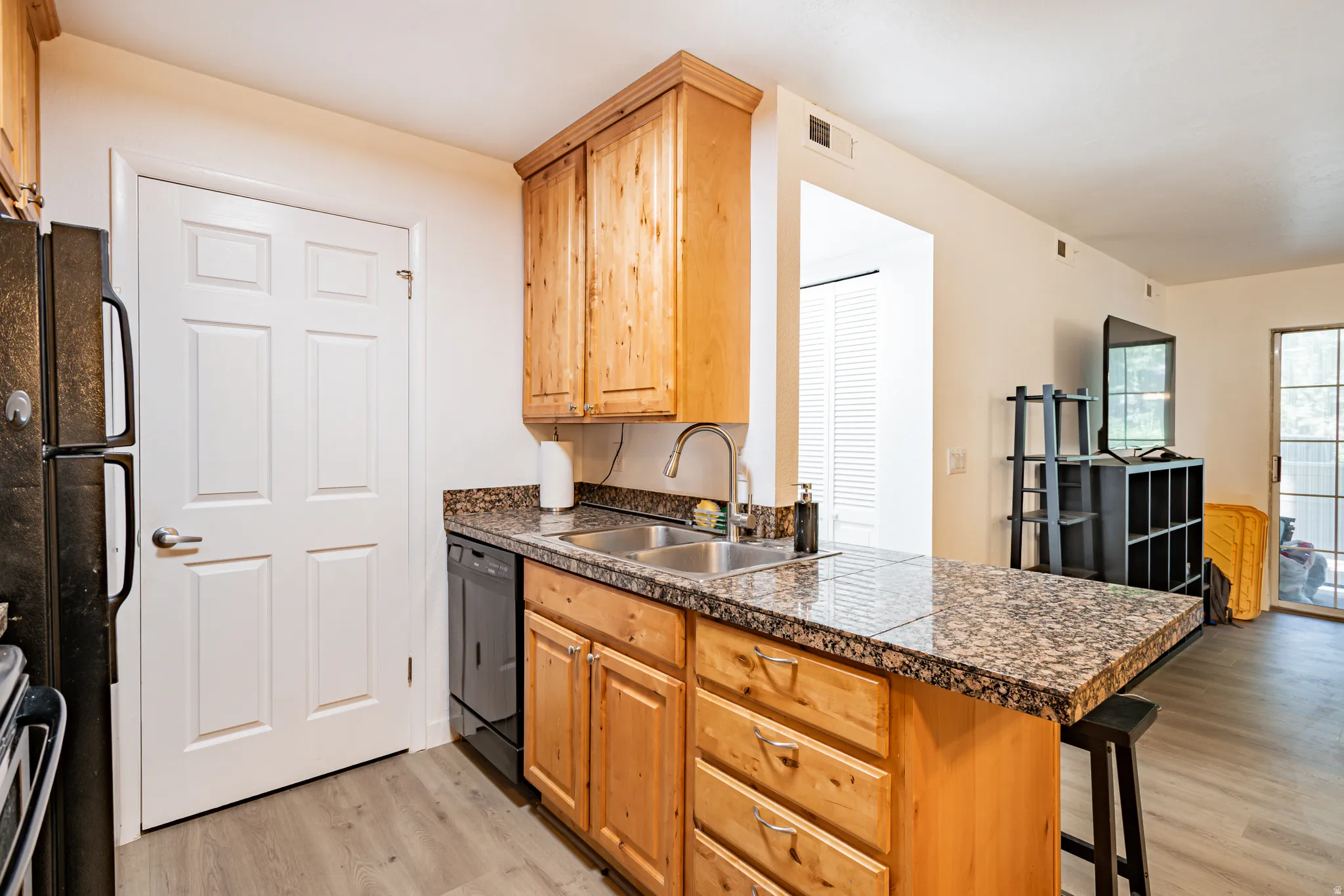 Kitchen featuring granite countertops, wood-finish cabinetry, a stainless steel sink, and a black dishwasher