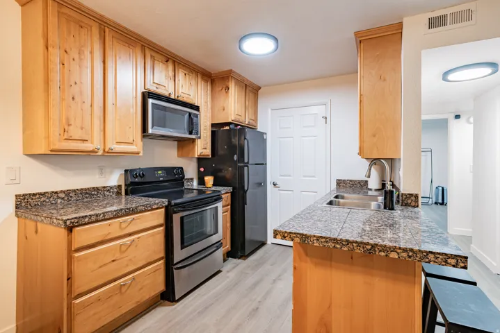 Kitchen featuring wood cabinetry, mottled countertop surfaces, stainless steel appliances, and wood-finish flooring
