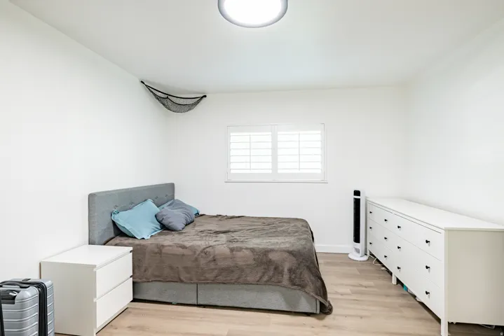 Bedroom featuring light wood-finish flooring and a window with white plantation shutters