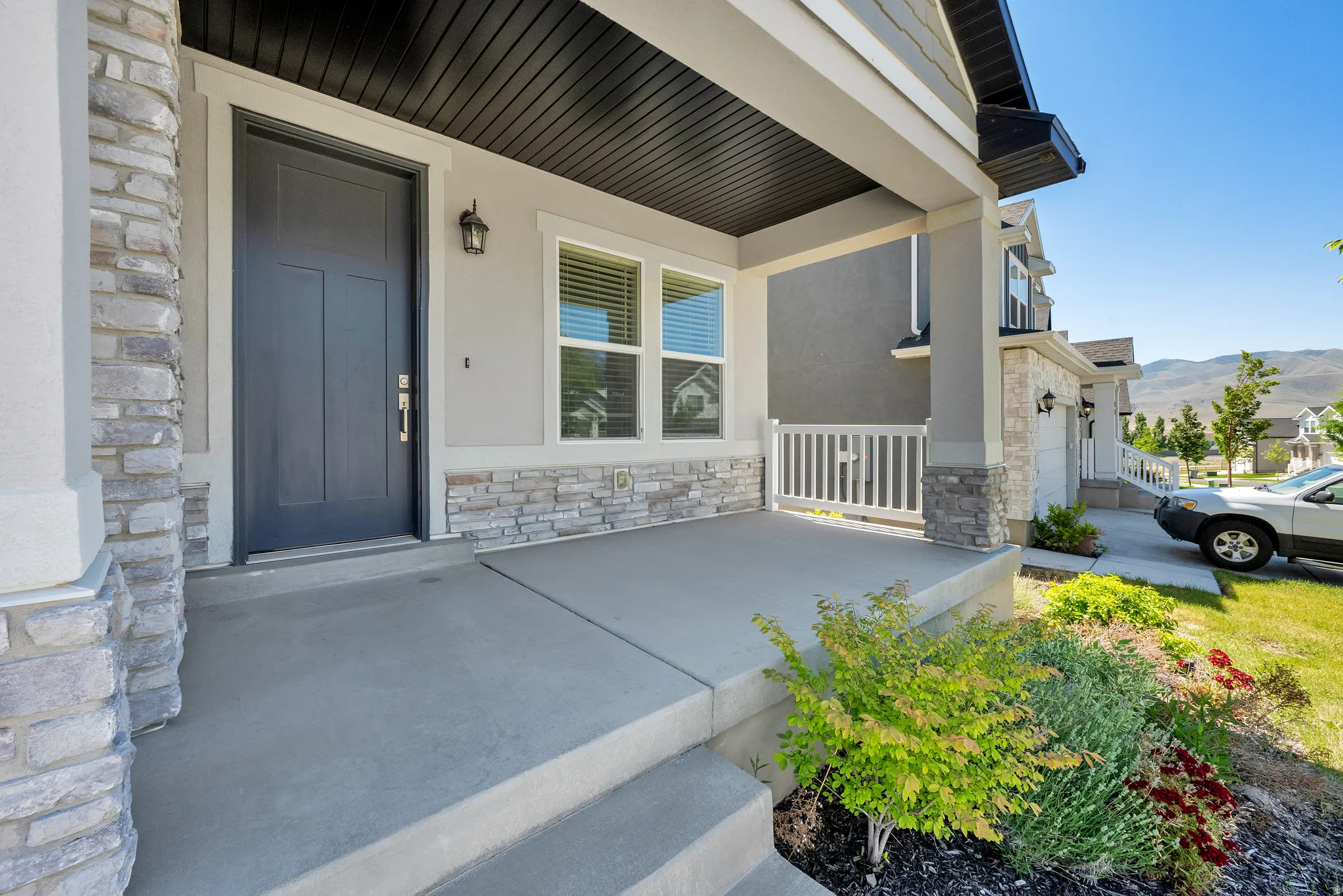 Covered front porch featuring stacked stone accents, a dark paneled entry door, and a white balustrade