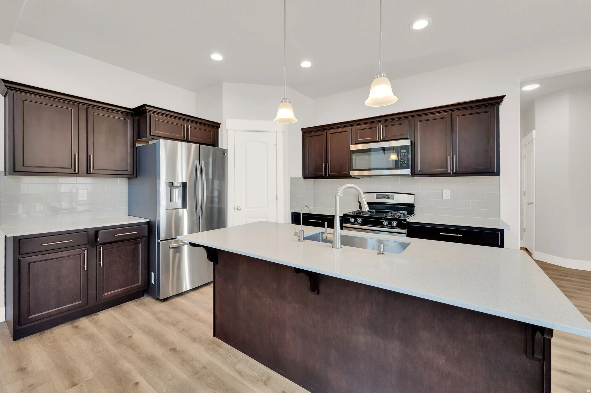 Kitchen featuring dark wood cabinetry, light countertops, light backsplash, stainless steel appliances, and wood-finish flooring