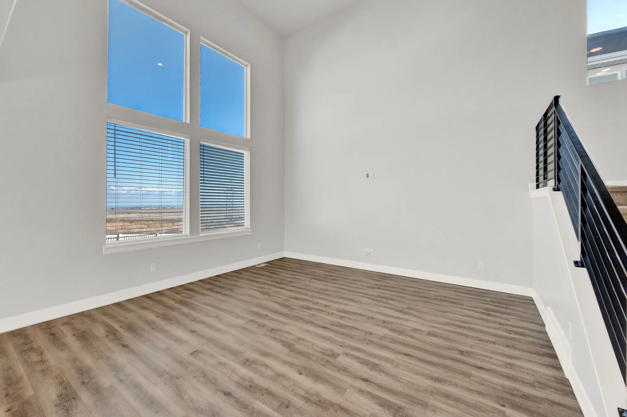 Two-story living area featuring wood-finish flooring, white baseboards, and a modern black metal staircase railing