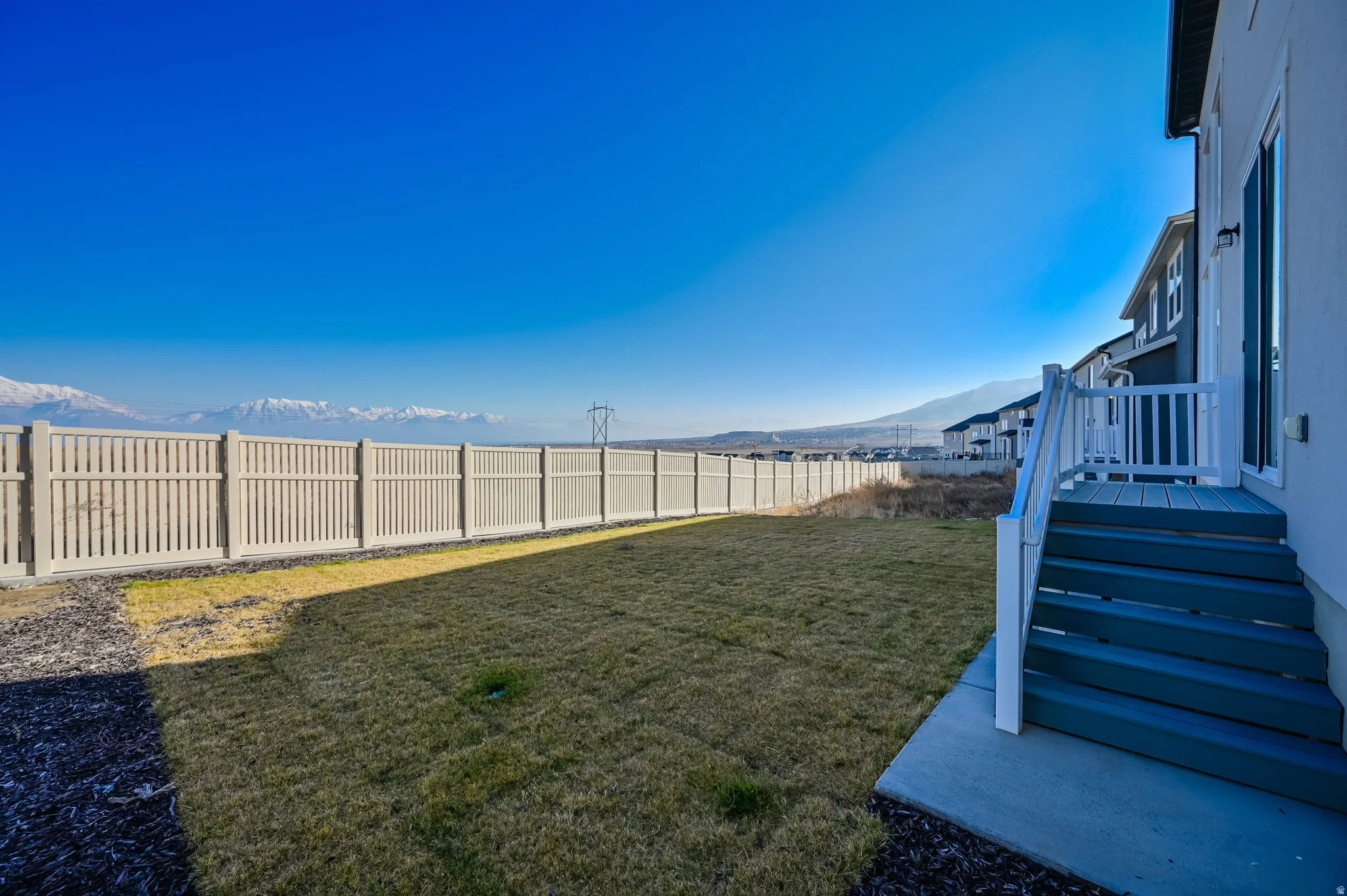 Rear yard featuring a full privacy fence, established lawn, and a deck with stairs providing outdoor access