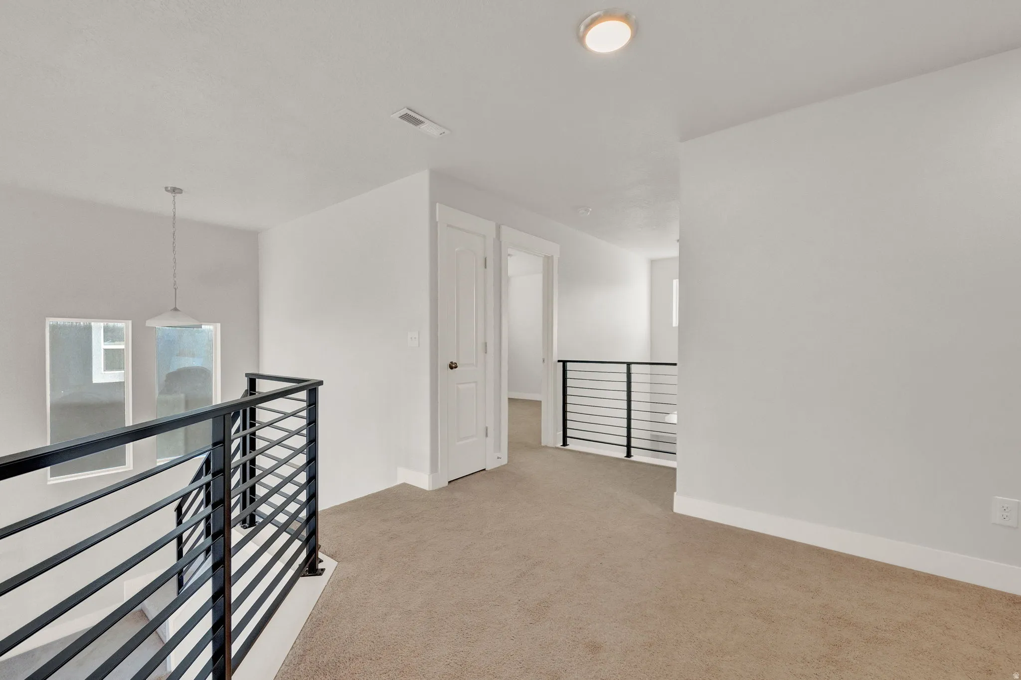 Open loft area with contemporary horizontal metal railings, neutral carpeting, white interior doors, and recessed lighting