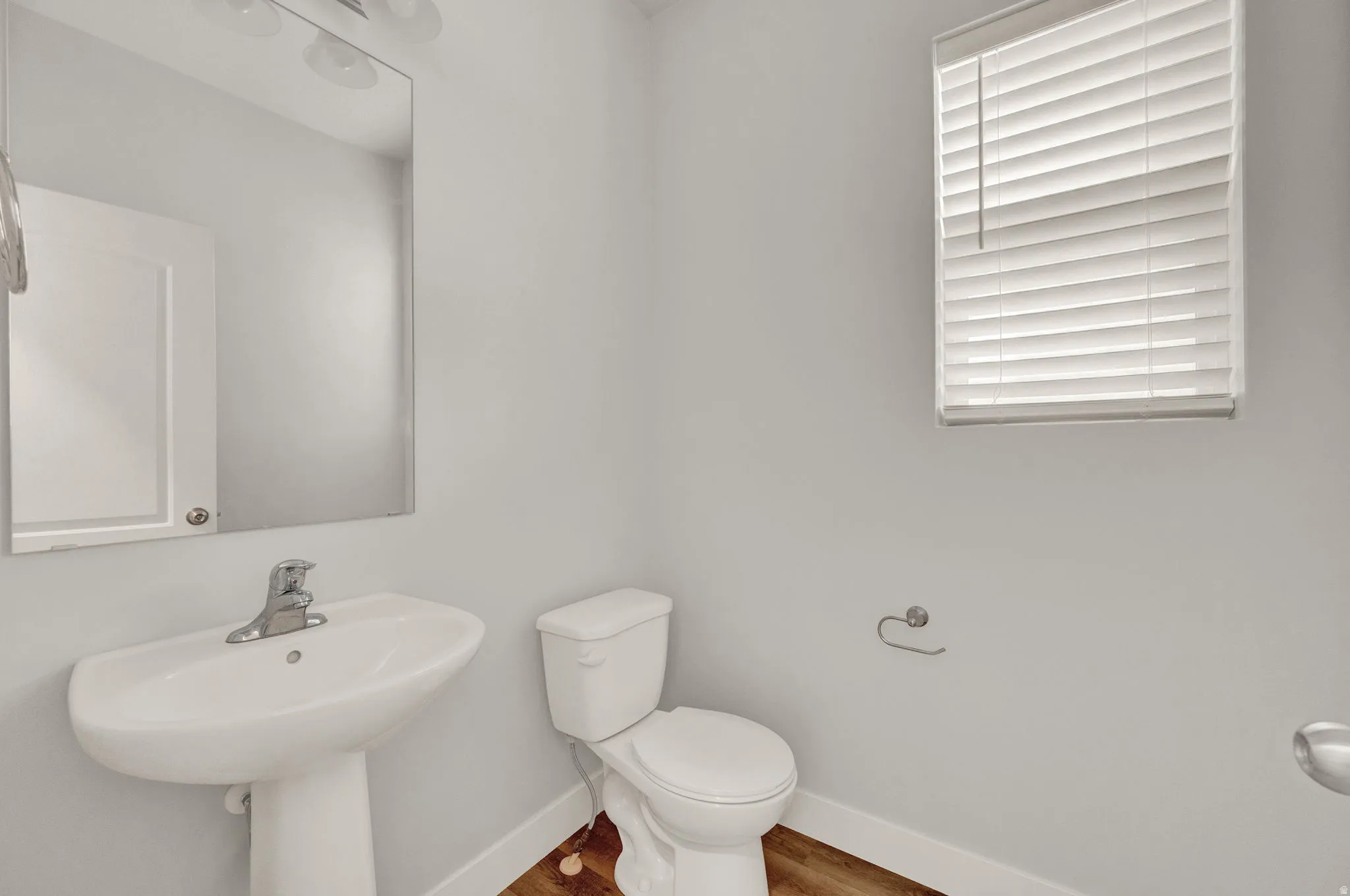 Pedestal sink with chrome faucet, large vanity mirror, and white toilet