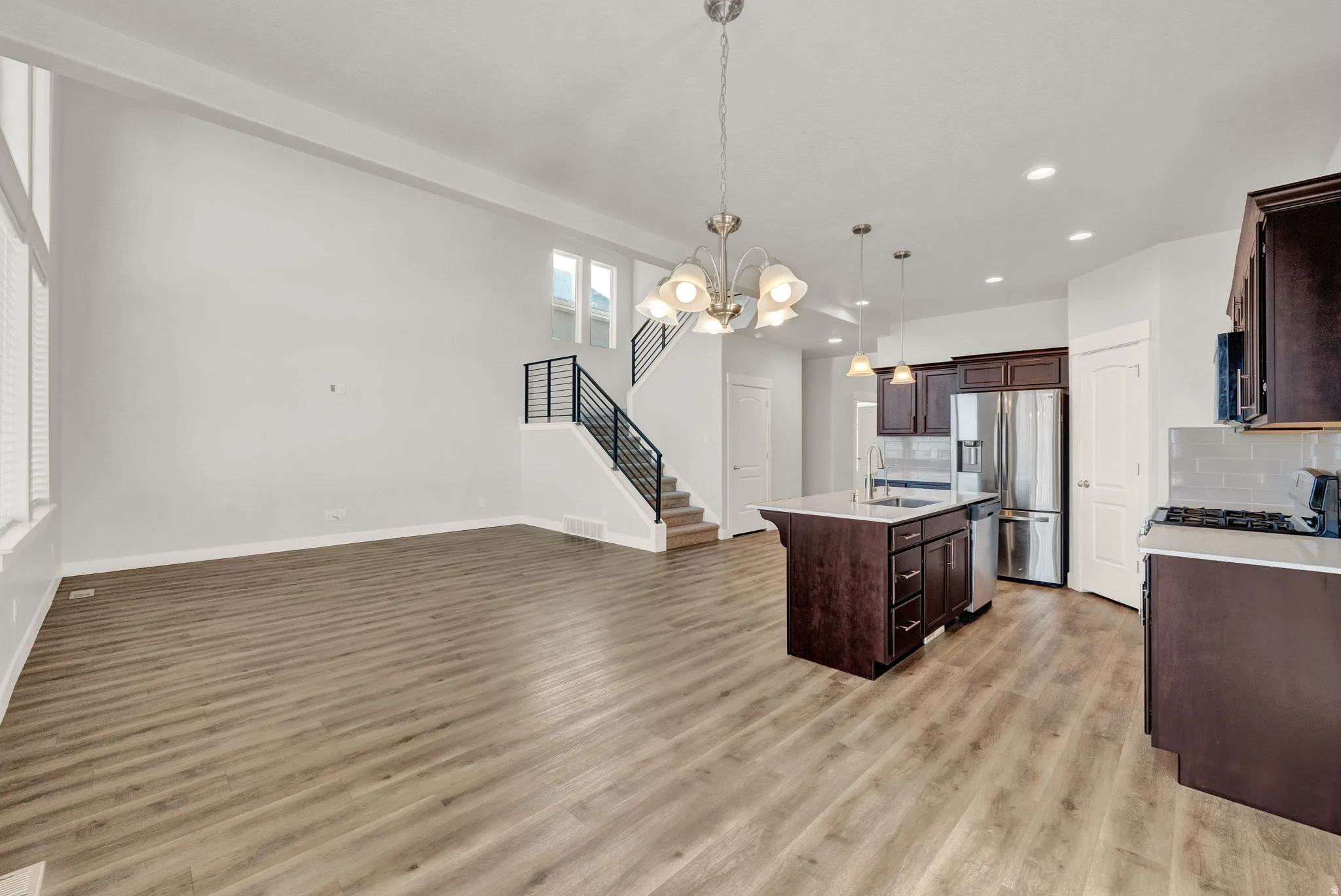 Open-concept living space featuring wood-finish flooring, a contemporary kitchen island with a sink, stainless steel appliances, and a modern staircase with dark railings