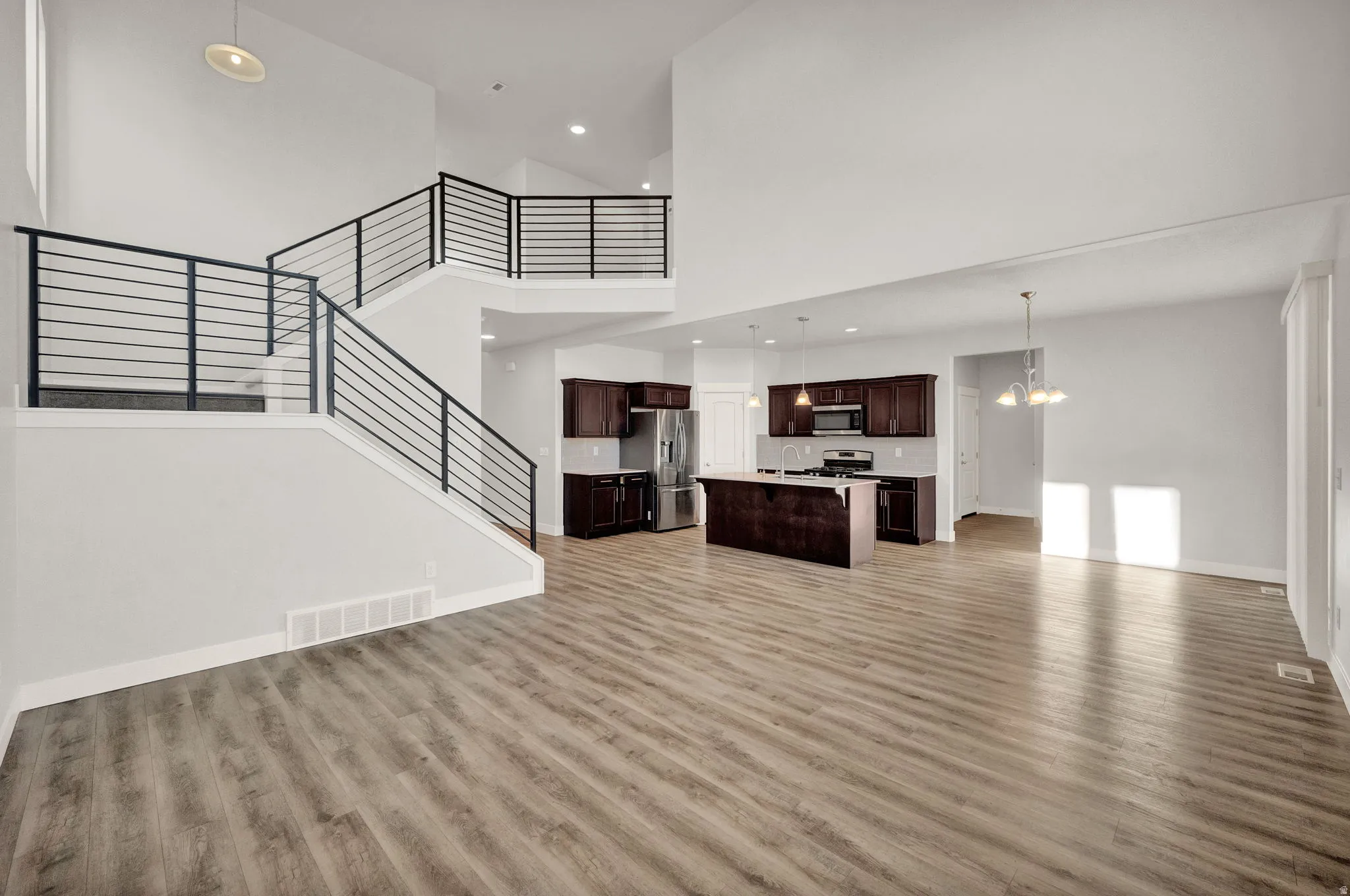 Open-concept living space featuring wood-finish flooring, a two-story ceiling, and a modern staircase with horizontal black railings