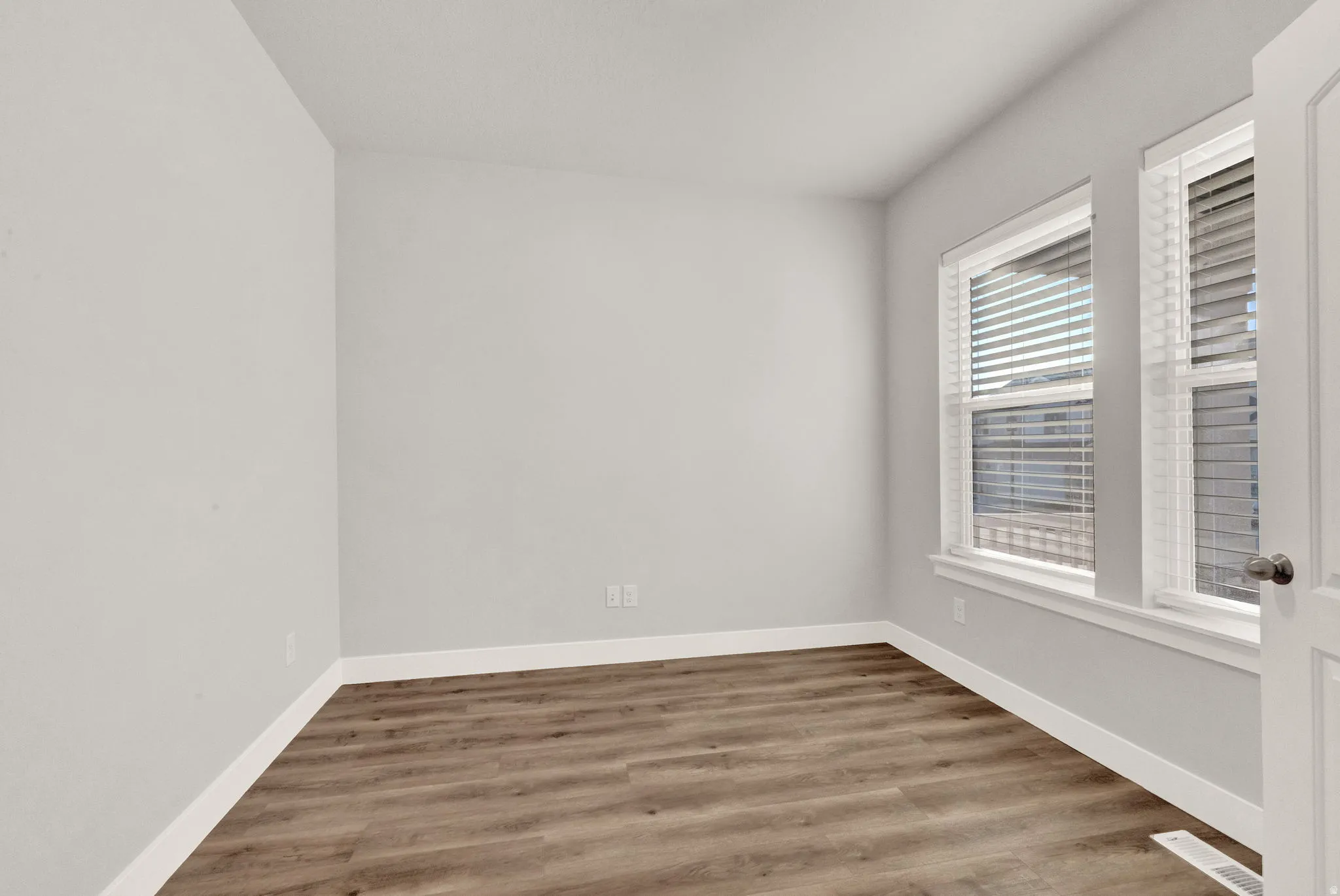 Bright interior space featuring wood-finish flooring, white baseboards, and two windows with blinds