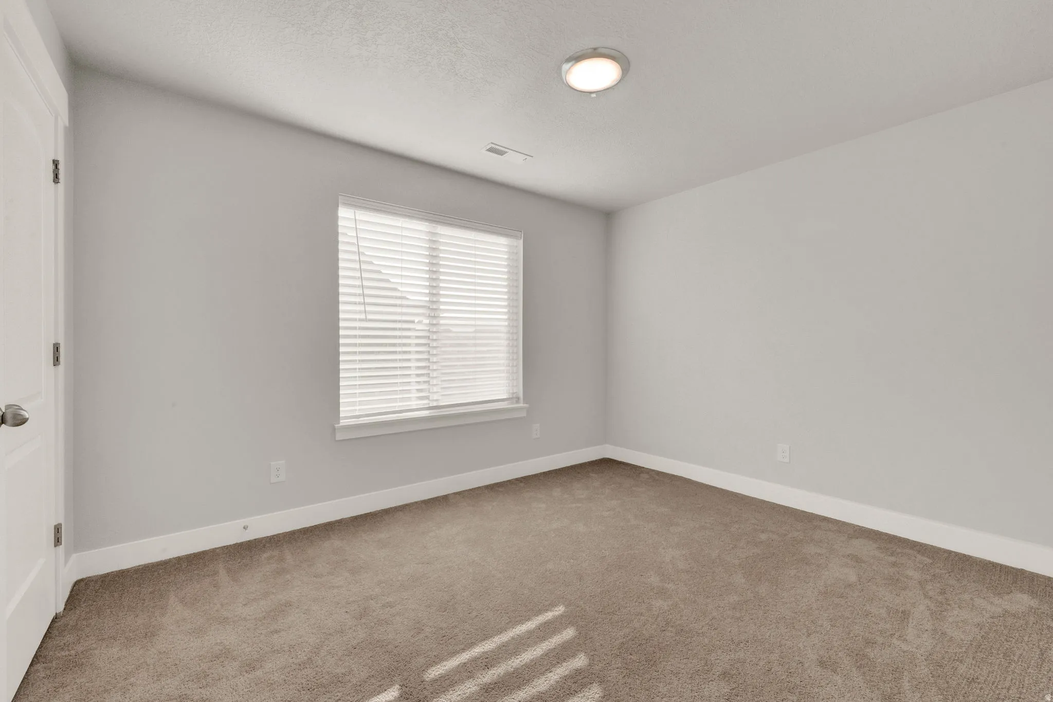 Carpeted room featuring a single window with horizontal blinds, white baseboards, and a flush-mount ceiling light fixture