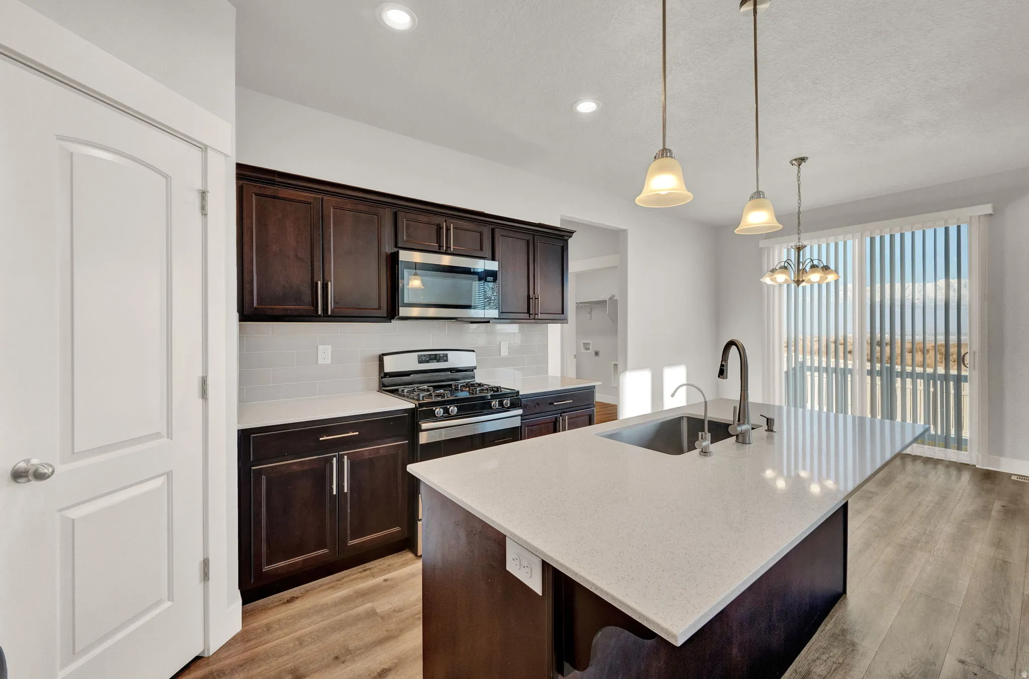 Modern kitchen featuring dark wood cabinetry, stainless steel appliances, a white subway tile backsplash, and a large island with an undermount sink and light-toned countertop