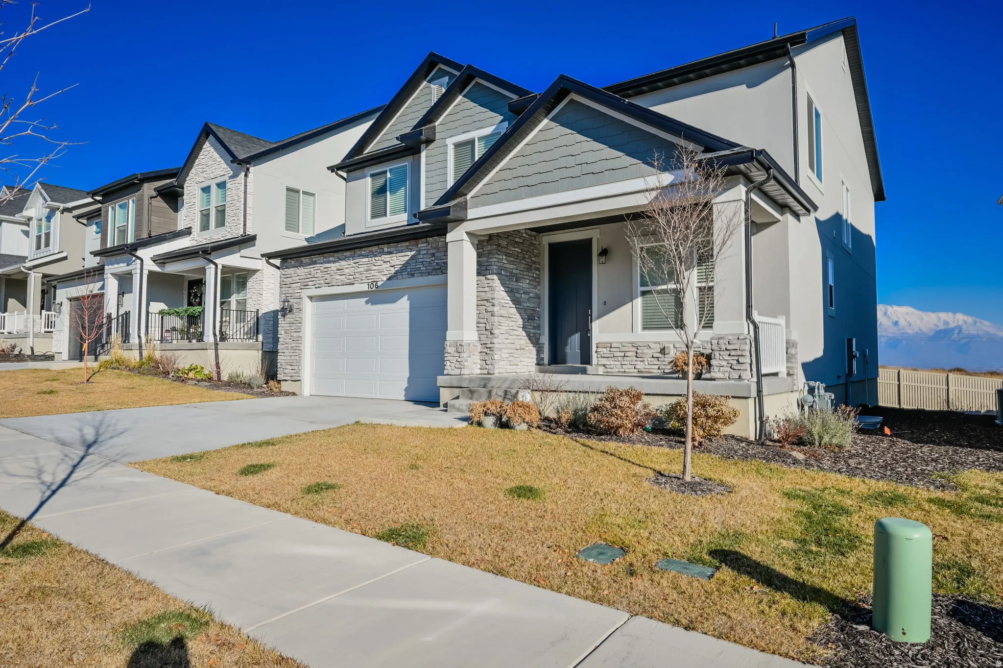 Contemporary residence featuring a covered front porch with stone pillars, a two-car garage, and a concrete driveway