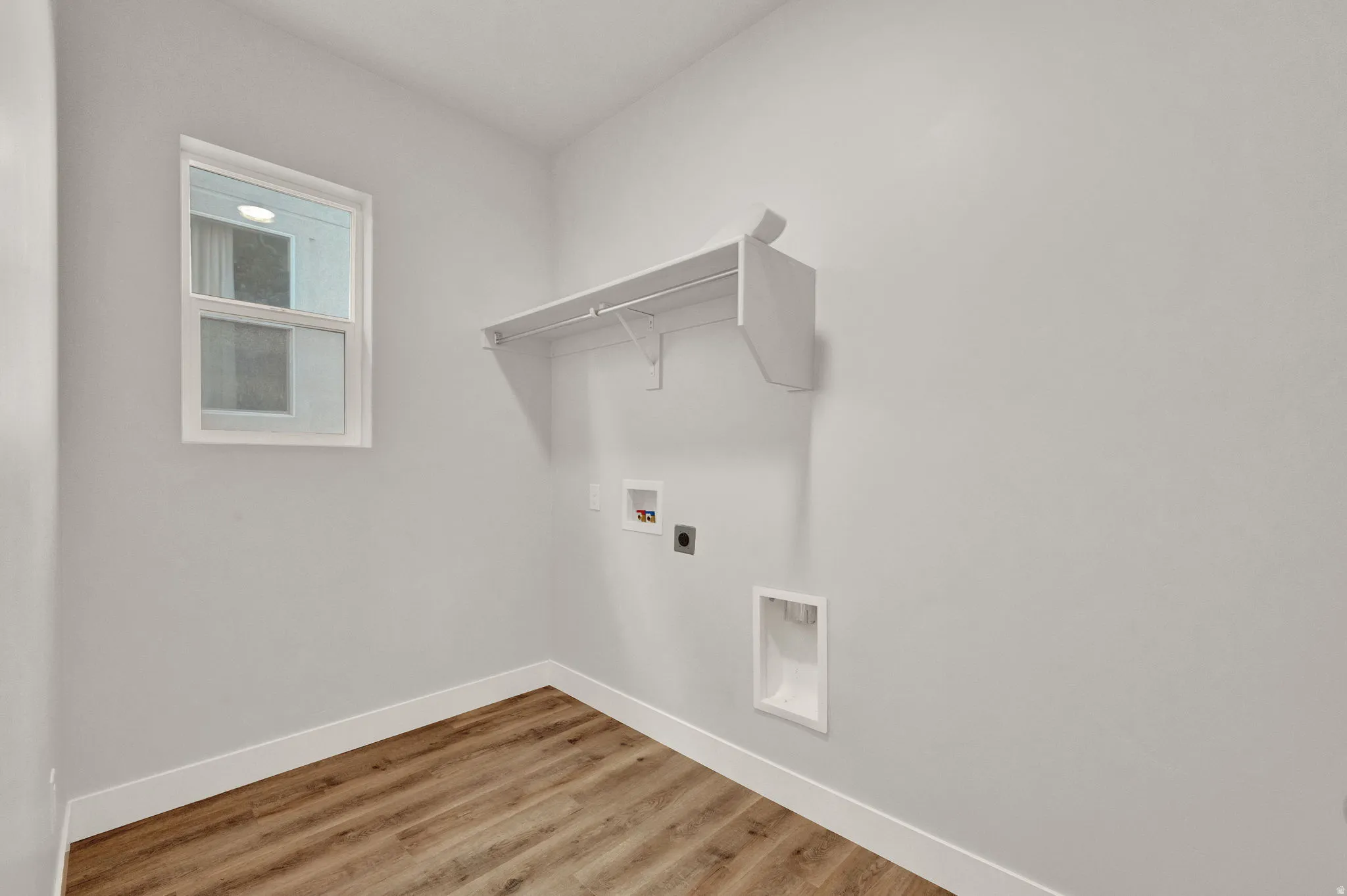 Dedicated laundry space featuring wood-finish flooring, a double-hung window, and a built-in shelf with hanging rod