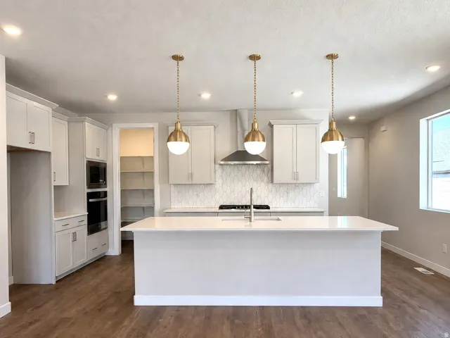 Modern kitchen featuring a large central island with a light-toned countertop, complemented by three brass pendant lights and recessed lighting. This image has been digitally staged or enhanced via artificial intelligence. These photos are for illustrativ