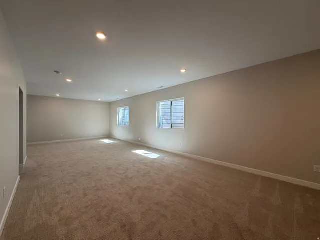 Spacious room with plush carpeting, neutral wall tones, multiple windows, recessed lighting, and white baseboards
