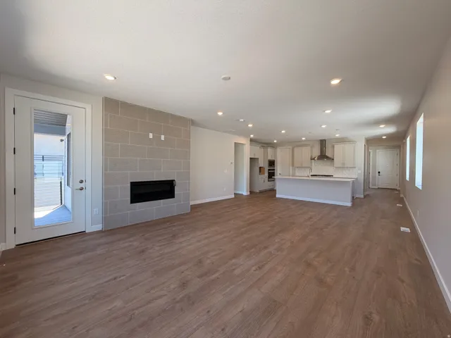 Spacious open-concept living area featuring wood-finish flooring, recessed lighting, and a modern fireplace with a light-toned brick surround