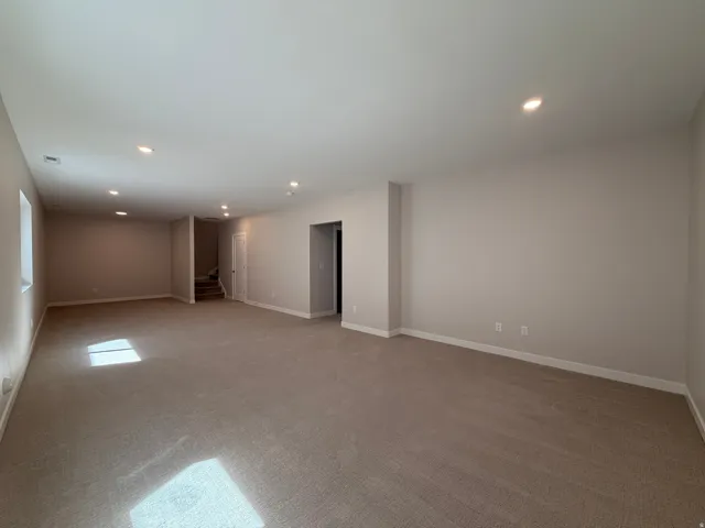 Expansive carpeted room featuring recessed lighting, neutral wall tones, white baseboards, and a window