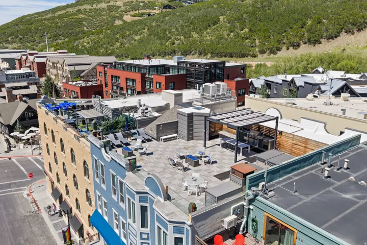 Expansive rooftop terrace featuring a pergola-covered outdoor kitchen, patterned paver flooring, multiple seating areas, and a surrounding privacy fence