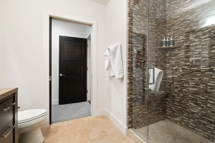 Glass-enclosed shower with mosaic tile surround, built-in shelving, and integrated bench