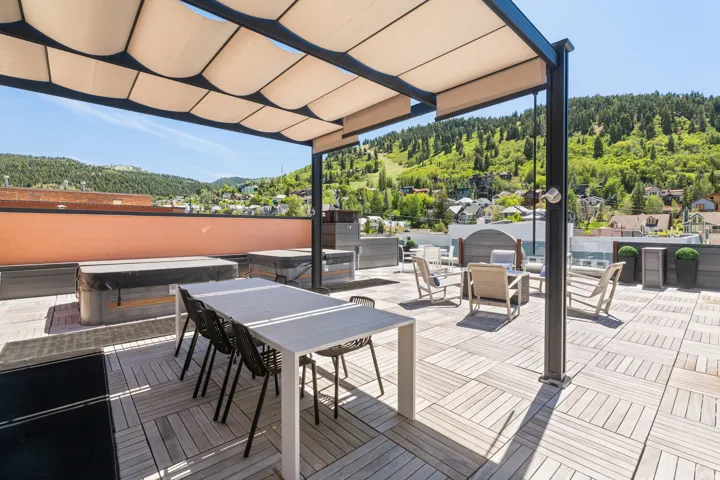 Rooftop patio featuring expansive tile flooring, a retractable shade structure, and multiple hot tubs