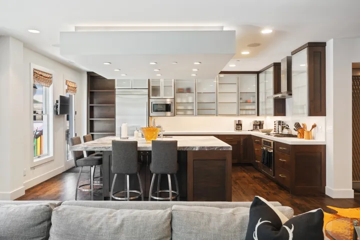 Gourmet kitchen featuring a large island with seating, stainless steel appliances, dark wood cabinetry, white countertops, and wood-finish flooring