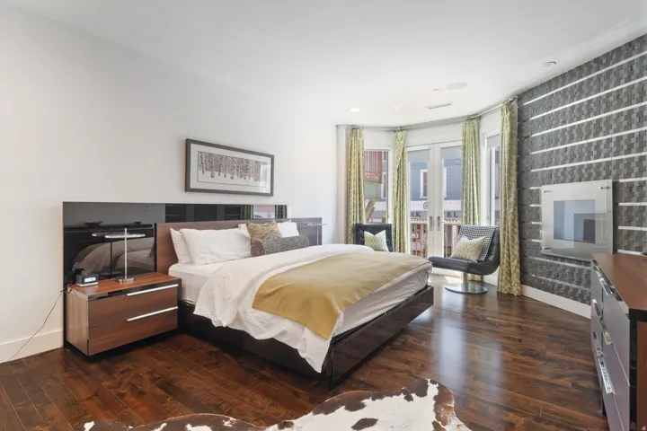 Spacious bedroom featuring dark wood-finish flooring, a curved wall with a built-in electric fireplace, and French doors opening to an exterior balcony