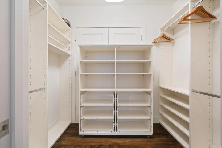 Walk-in closet featuring white built-in shelving, hanging rods, and dark wood-finish flooring