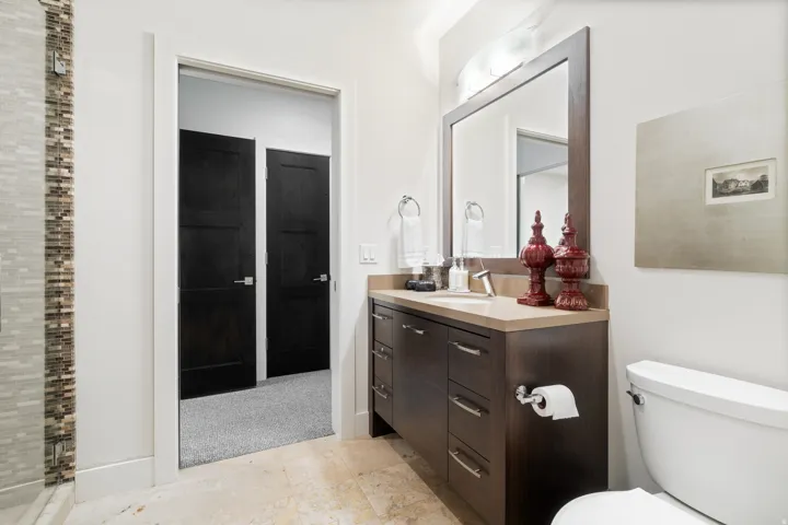 Bathroom featuring a dark wood-finish vanity with a light countertop, a framed mirror, a toilet, and tile flooring