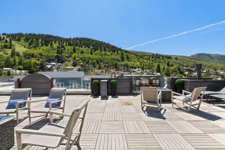 Expansive rooftop deck featuring modular wood-finish flooring, a contemporary privacy wall, a built-in fire feature, and a glass railing system overlooking a mountainous landscape